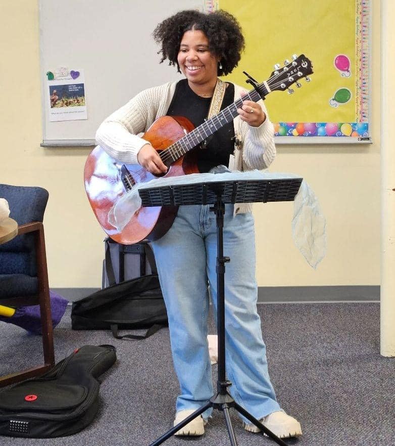 Raven holding guitar leading a music therapy group